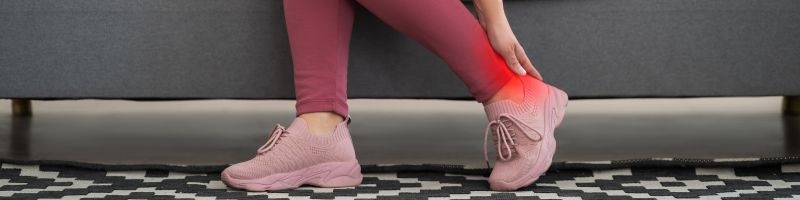 hielspoor Iemand met roze sneakers en een roze legging houdt een pijnlijk, rood verlichte hiel en enkel vast.